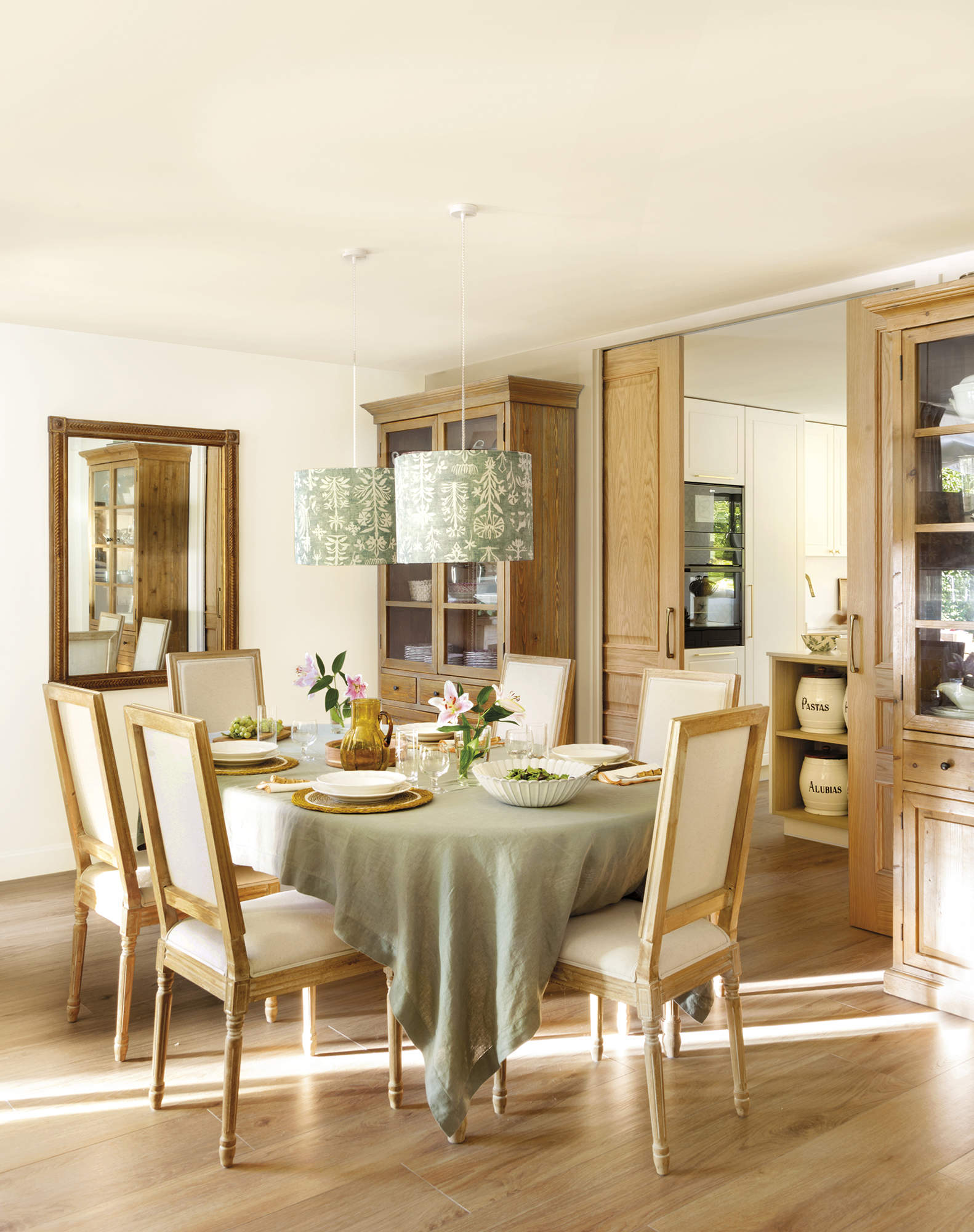 Comedor con mesa con mantel verde y sillas de madera tapizadas, espejo, vajilla blanca, suelo de madera